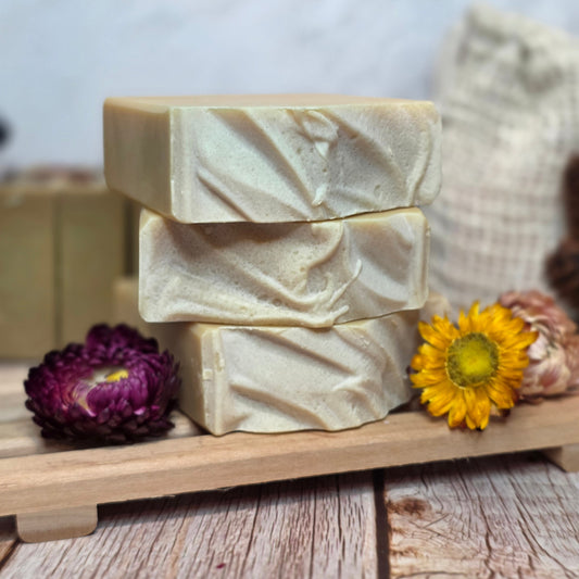 Three bars of soap in a wooden tray with a sunflower and purple flower on a wooden surface.