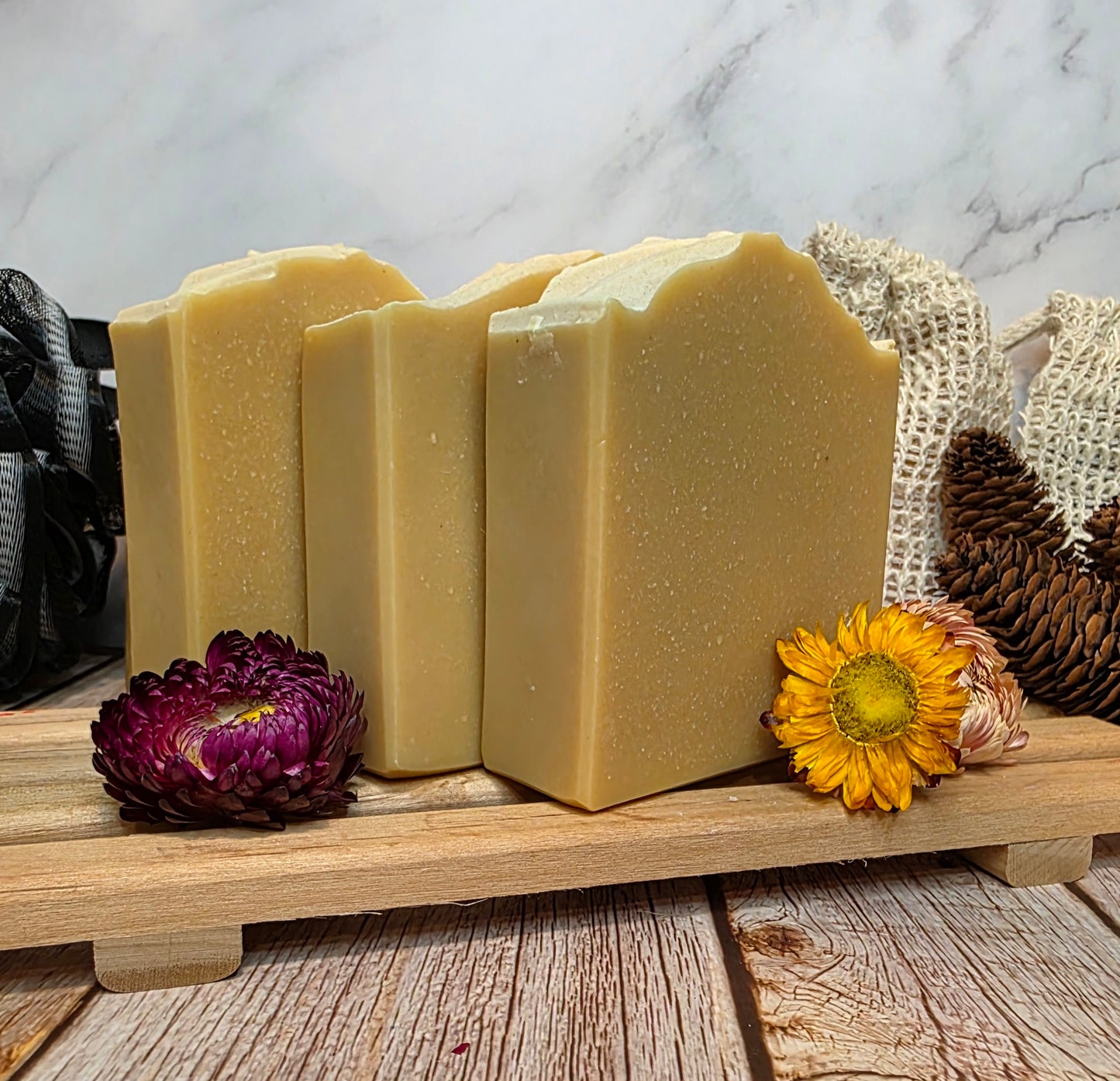 Three bars of soap on a wooden stand with decorative flowers and a textured background