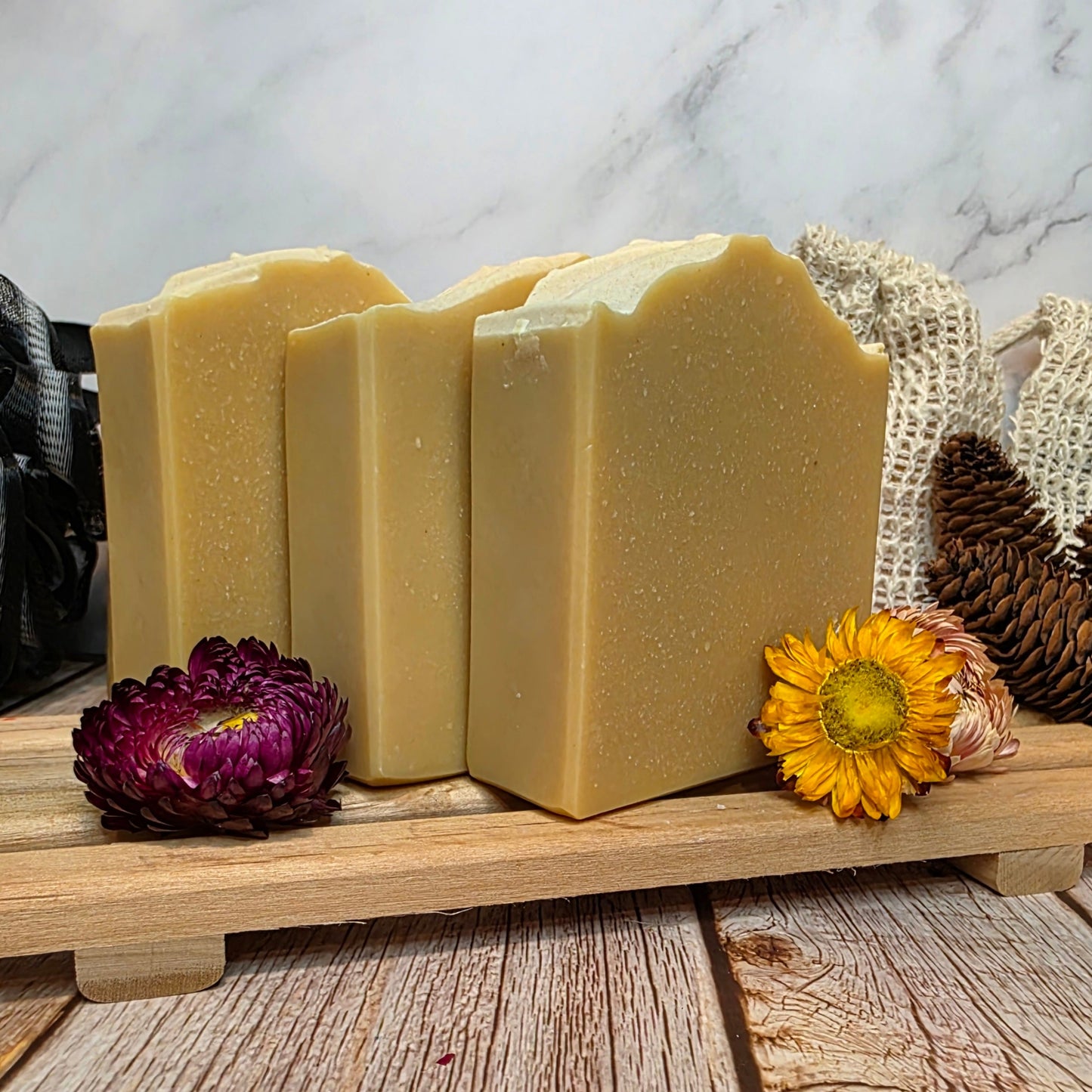 Three bars of soap on a wooden stand with decorative flowers and a textured background