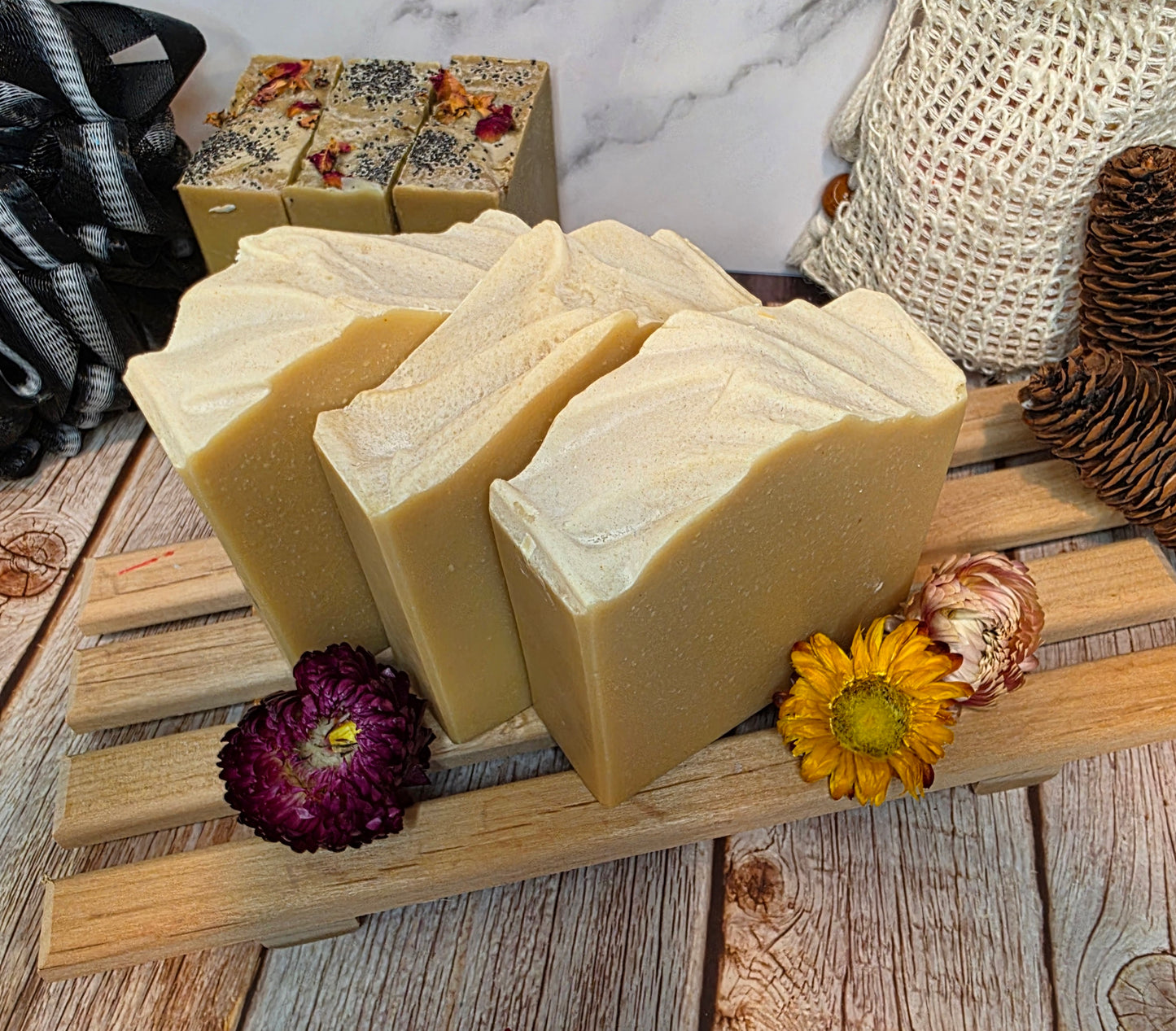 Three bars of soap on a wooden stand with decorative flowers on a rustic wooden surface.