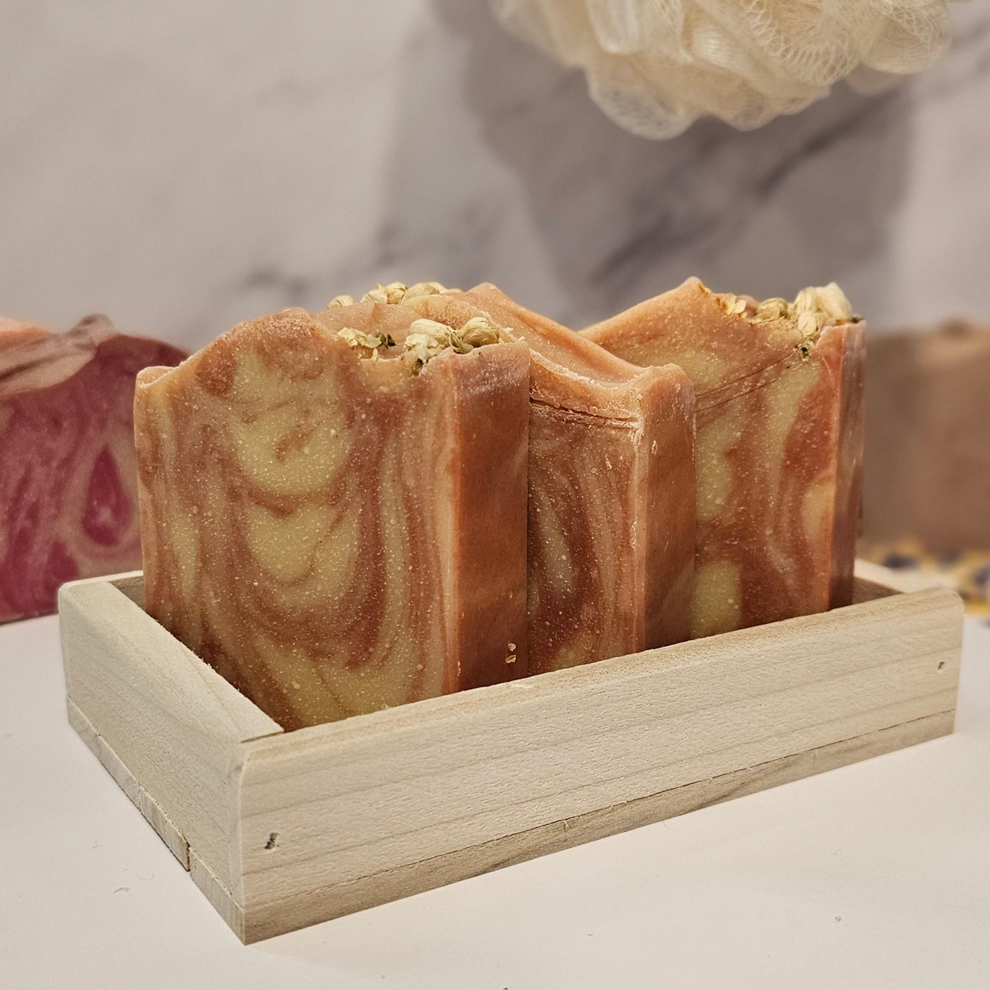 Bars of soap with a swirled pattern and a beige top, arranged in a wooden tray.