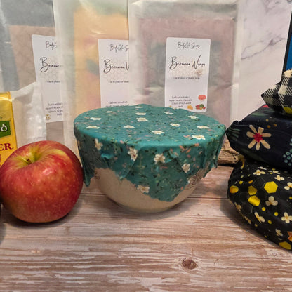 100% cotton beeswax wrapped bowl with floral pattern on a wooden surface, next to an apple and a package.