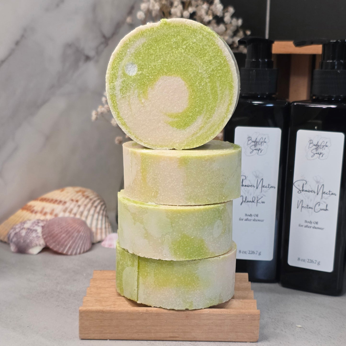 Four round bath salts stacked on a small wooden block, with one round standing upright on top. The bath salts are light green and cream marbled.