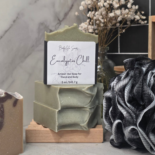 A handmade bar of soap labeled 'Eucalyptus Chill' by BodyGlo Soap, displayed on a wooden stand. The soap is a muted sage green color with a white paper label.