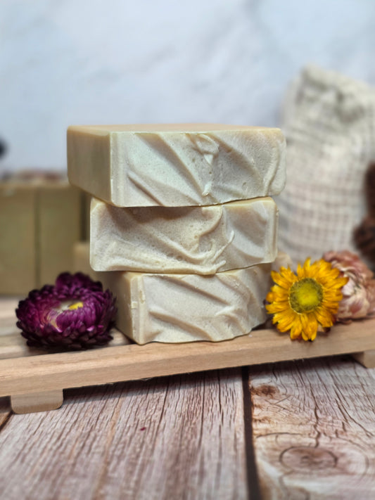 Three bars of soap in a wooden tray with a sunflower and purple flower on a wooden surface.