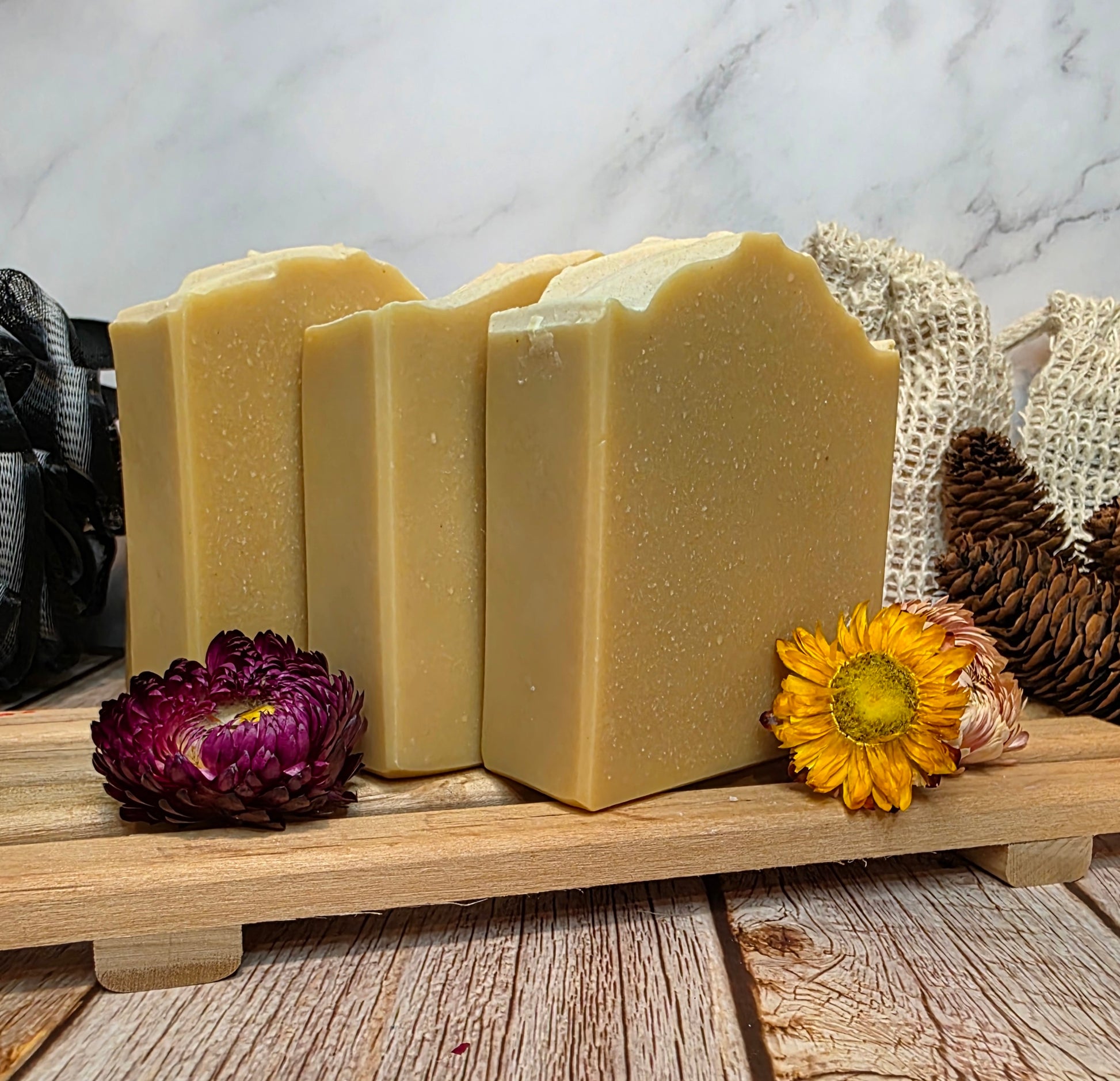 Three bars of soap on a wooden stand with decorative flowers and a textured background