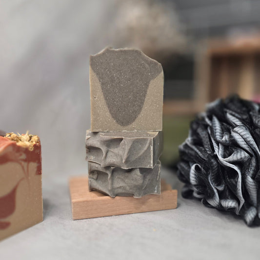 A handmade gray soap bar with a textured, layered design displayed on a small wooden stand on a gray surface.